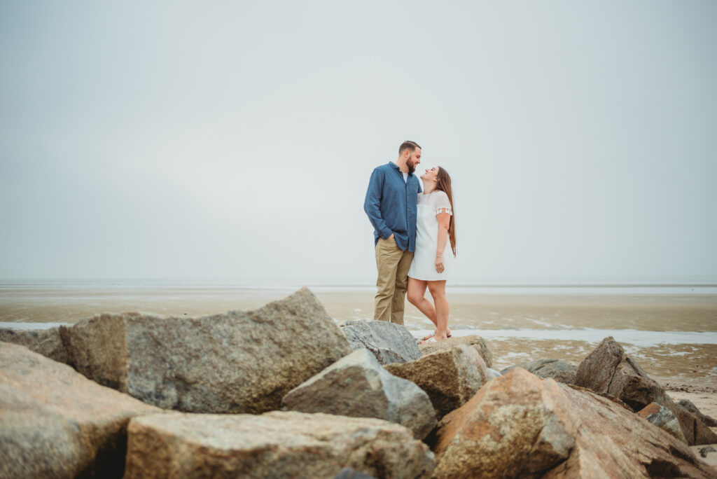 Happy couple embracing at sunset during their engagement photo session at Crosby Landing Beach in Brewster, Massachusetts, captured by Sarah Murray Photography