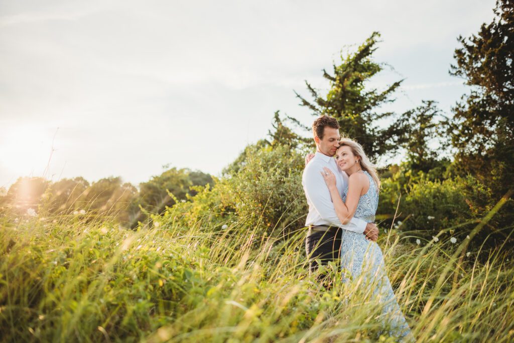 Engaged couple embracing during a stunning sunset at Ned's Point Lighthouse in Mattapoisett, Massachusetts, capturing their love in a picturesque coastal setting